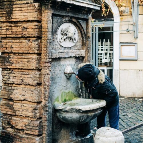 person drinking form a water fountain in rome