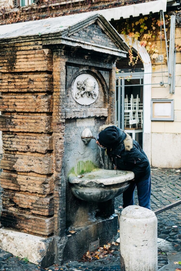 person drinking form a water fountain in rome